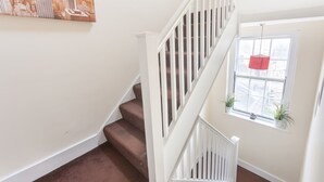Eine Treppe mit weißen Geländern und braunen Stufen, ein Fenster mit Pflanzen und ein Stadtbild als Wandgemälde.