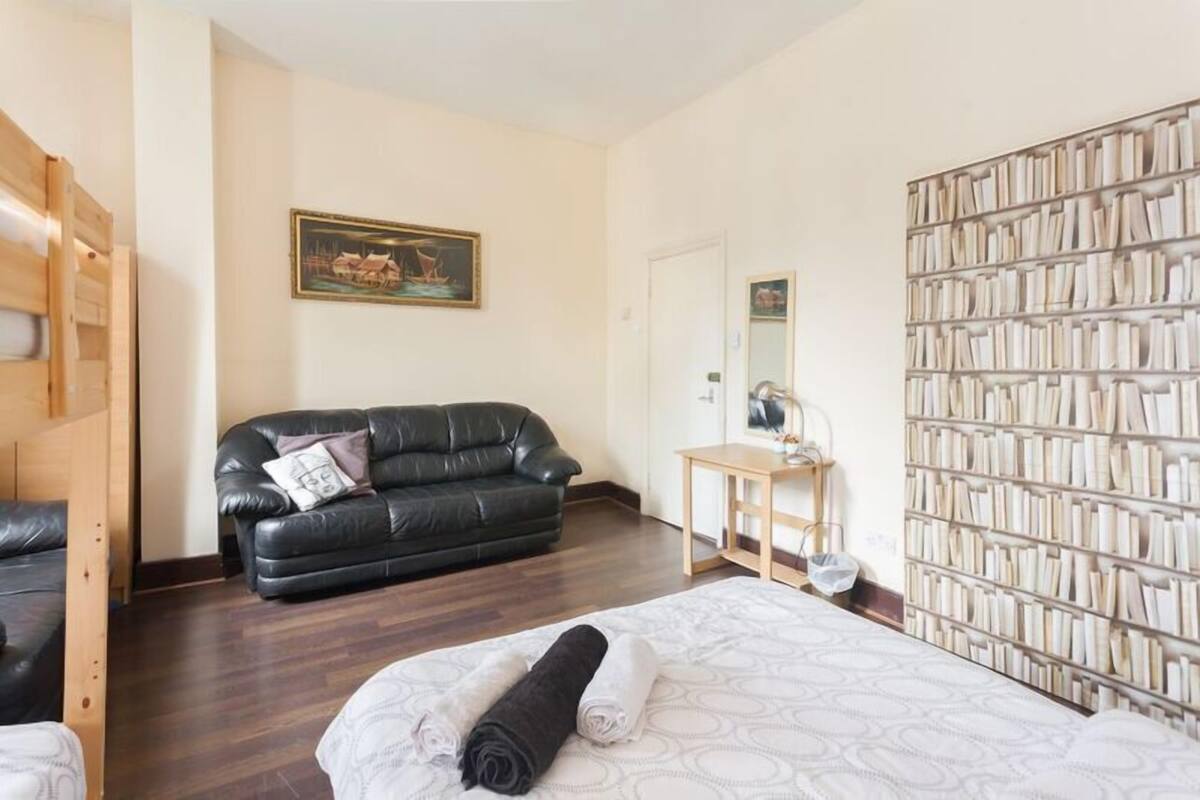 A bedroom with a bed, a black leather sofa, a small table with a mirror, and a bookshelf.