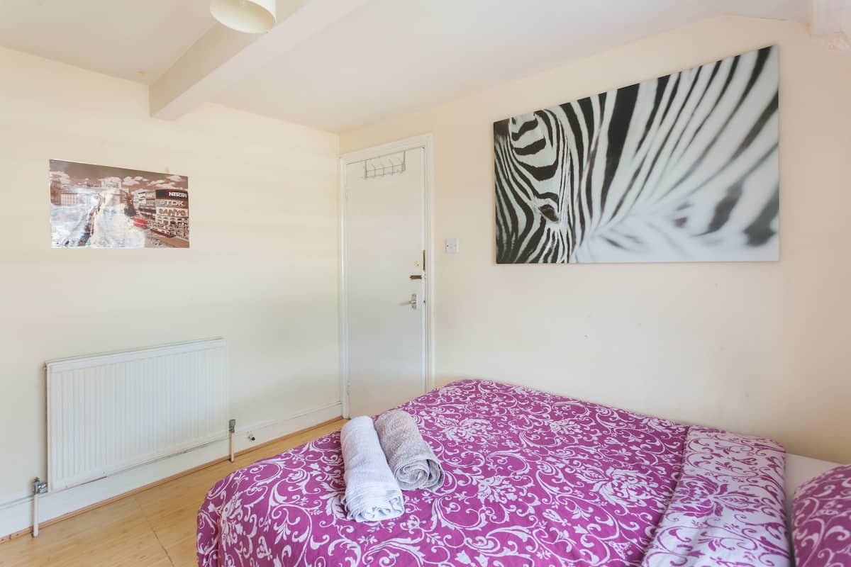 A bedroom with a bed, a radiator, a door, and two wall art pieces.