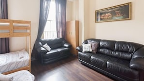 Ein Zimmer mit einem Etagenbett, zwei schwarzen Ledersofas, einem Holzschrank und einem Bild an der Wand.