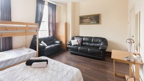 Ein Zimmer mit einem Etagenbett, einem schwarzen Ledersofa, einem Holztisch und einem Bild an der Wand.