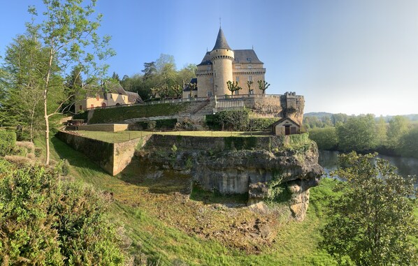 A castle on a cliff overlooking a river, with a tower and multiple buildings.