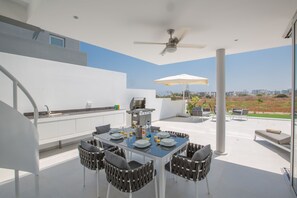 An outdoor dining area with a table set for four, surrounded by chairs, a ceiling fan, and an umbrella. - Villa Alana, Stunning 3BDR Protaras Villa with Heated Pool, Close to the Beach (Protaras)