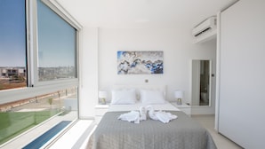 Quarto de hotel moderno com uma cama grande, um quadro na parede e vista para a cidade pela janela.