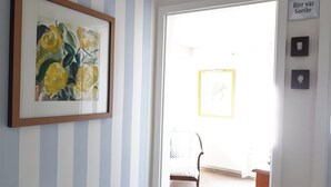 A room with a framed painting of yellow flowers on the wall, a door leading to another room, and a sign that reads "Hier war Goethe". - Ferienwohnung Amsel (Lübbenau/Spreewald)