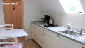 A small kitchenette with a white table, a chair, a coffee maker, and a sink. - Ferienwohnung Amsel (Lübbenau/Spreewald)