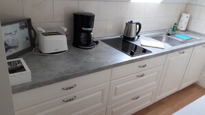A kitchen with a toaster, coffee maker, kettle, and a sink. - Ferienwohnung Amsel (Lübbenau/Spreewald)