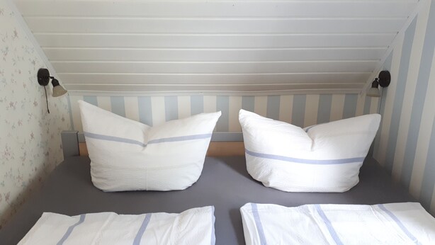 A small, single-room bed with striped wallpaper and two bedside lamps. - Ferienwohnung Amsel (Lübbenau/Spreewald)