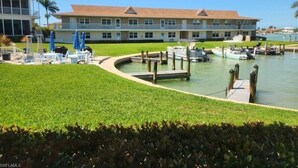 Un puerto deportivo con barcos amarrados, una zona ajardinada y un edificio con varios balcones.