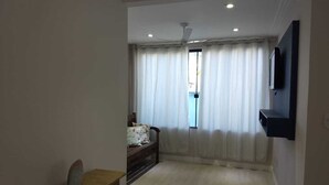 Un salon spacieux doté d’une grande fenêtre, d’un ventilateur de plafond et d’un téléviseur à écran plat fixé au mur.