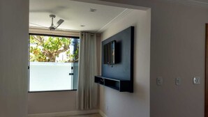 Une pièce dotée d’un ventilateur de plafond, d’un téléviseur fixé au mur et d’une fenêtre avec des rideaux.