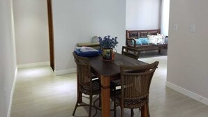 Un coin repas avec une table en bois et des chaises en osier, une petite plante posée sur la table et un canapé à l’arrière-plan.