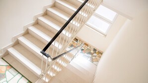 A staircase with a black handrail and beige steps leading to a landing with a tiled floor. - Wind Rose Split (Split)
