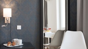 A room with a large mirror, a bedside table with a lamp, a chair, and a view of a dining area. - Wind Rose Split (Split)