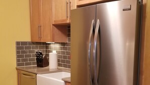 Una cocina con armarios de madera, un refrigerador de acero inoxidable, una encimera blanca y un salpicadero de azulejos.
