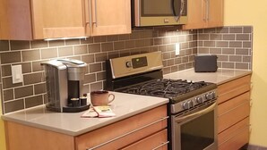 Una cocina con armarios de madera, microondas, estufa, cafetera y tostadora.