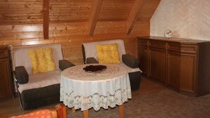 A cozy room with a wooden ceiling, two sofas with cushions, a small round table with a lace tablecloth, and a cabinet.