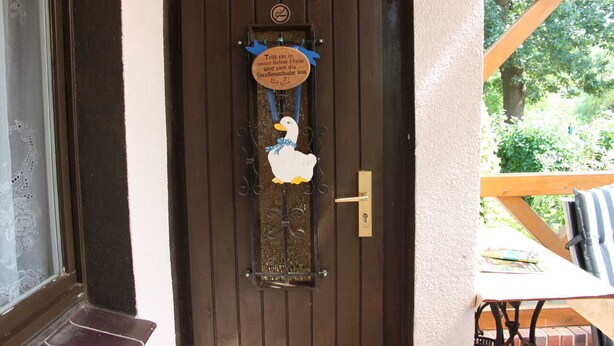 A door with a decorative duck sign and a window with a view of greenery.