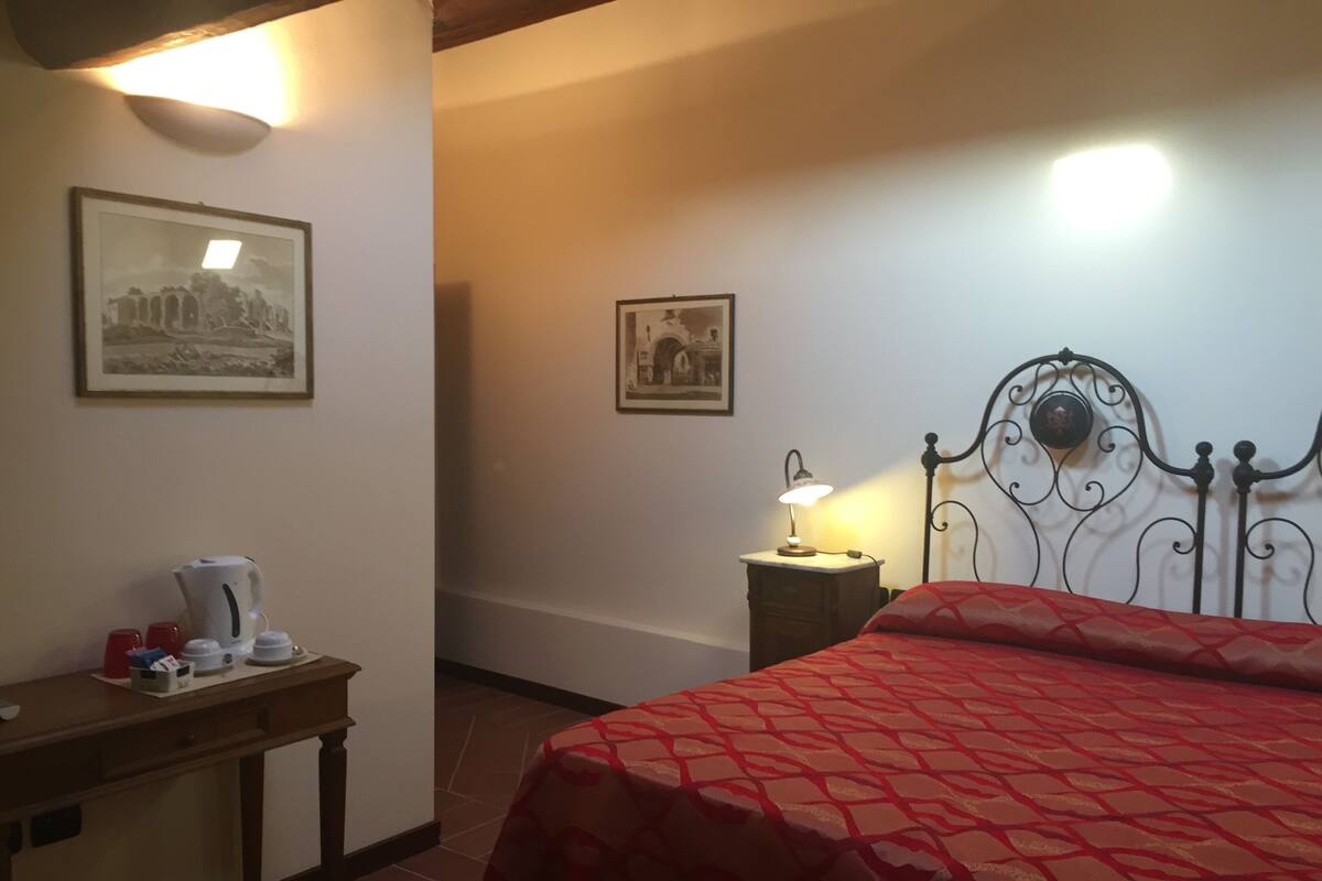 Ein Hotelzimmer mit einem Bett, einem Schreibtisch mit Wasserkocher und zwei gerahmten Bildern an der Wand.