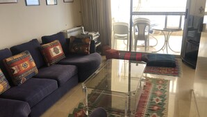 A living room with a sofa, a glass coffee table, and a patterned rug. There is a radiator, a television, and a window with curtains. - Splendid Valley & Sea View (Broumana)