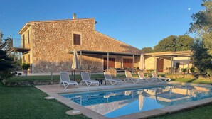 A stone building with a swimming pool, lounge chairs, and a covered patio area. - Modern house with large pool  (Búger)