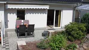 A house with a patio area featuring a table and chairs, a small garden, and a sliding glass door.