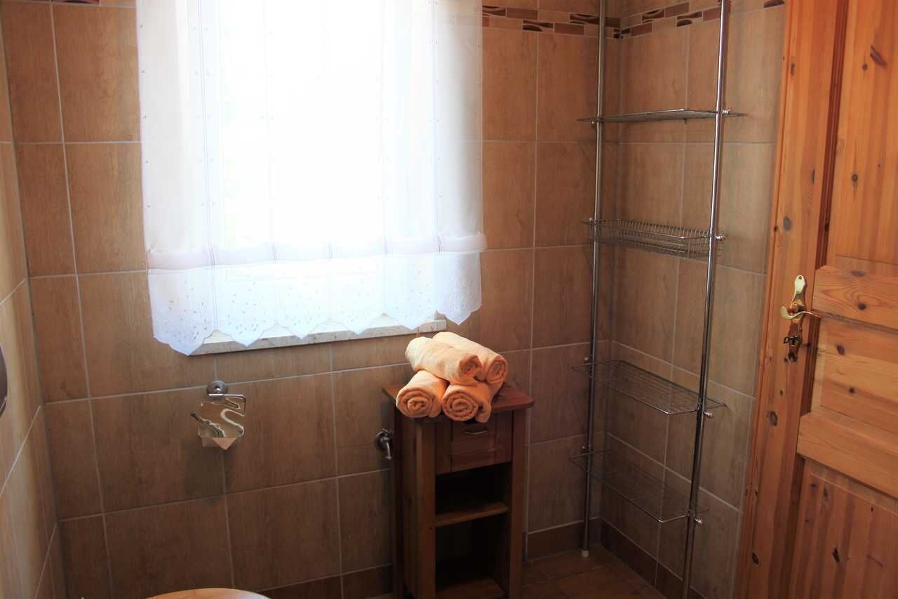 Un baño pequeño con ducha, una ventana con cortina y un perchero con toallas.