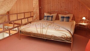 A bedroom with a metal bed frame, wooden walls, a small bedside table with a lamp, and a wooden railing.