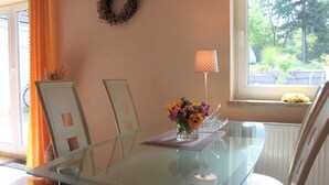 A dining area with a glass table, chairs, a vase with flowers, a lamp, and a view of the outdoors.