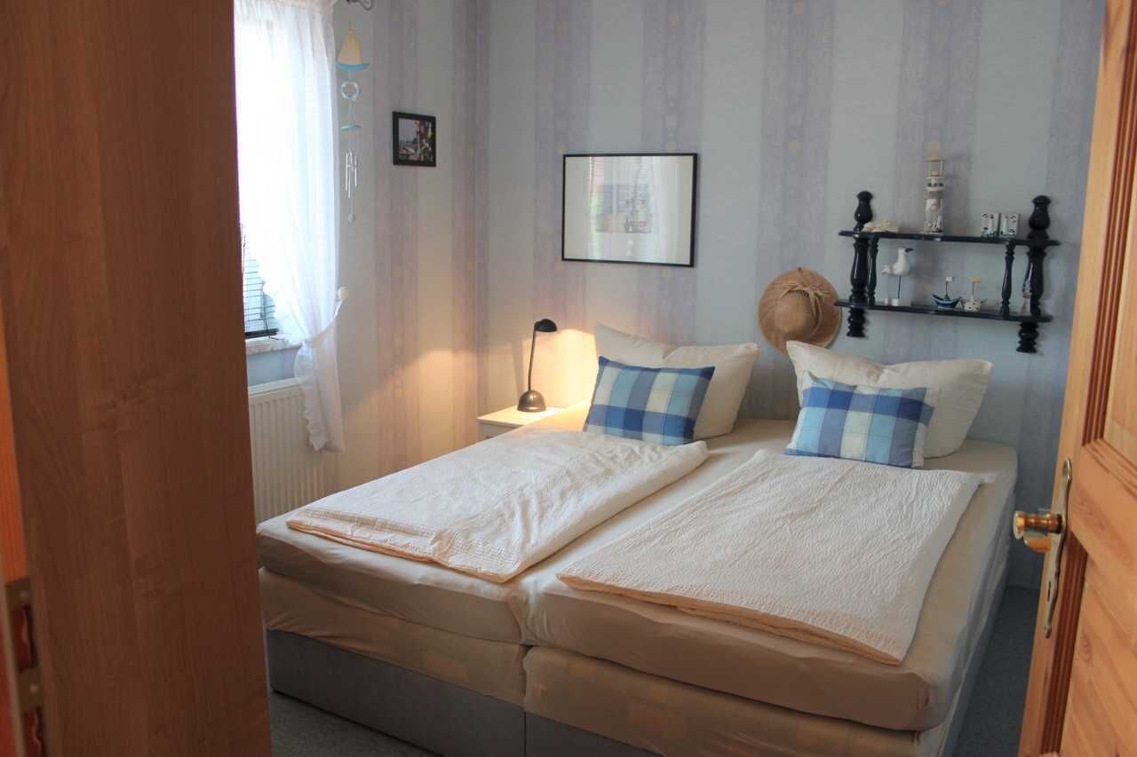 Quarto com duas camas, uma mesa de cabeceira com abajur, um quadro na parede e uma estante com objetos decorativos.