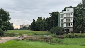 A modern building with a flat roof and multiple windows, surrounded by lush greenery and a golf course. - The Green' Apartments (Colombo)