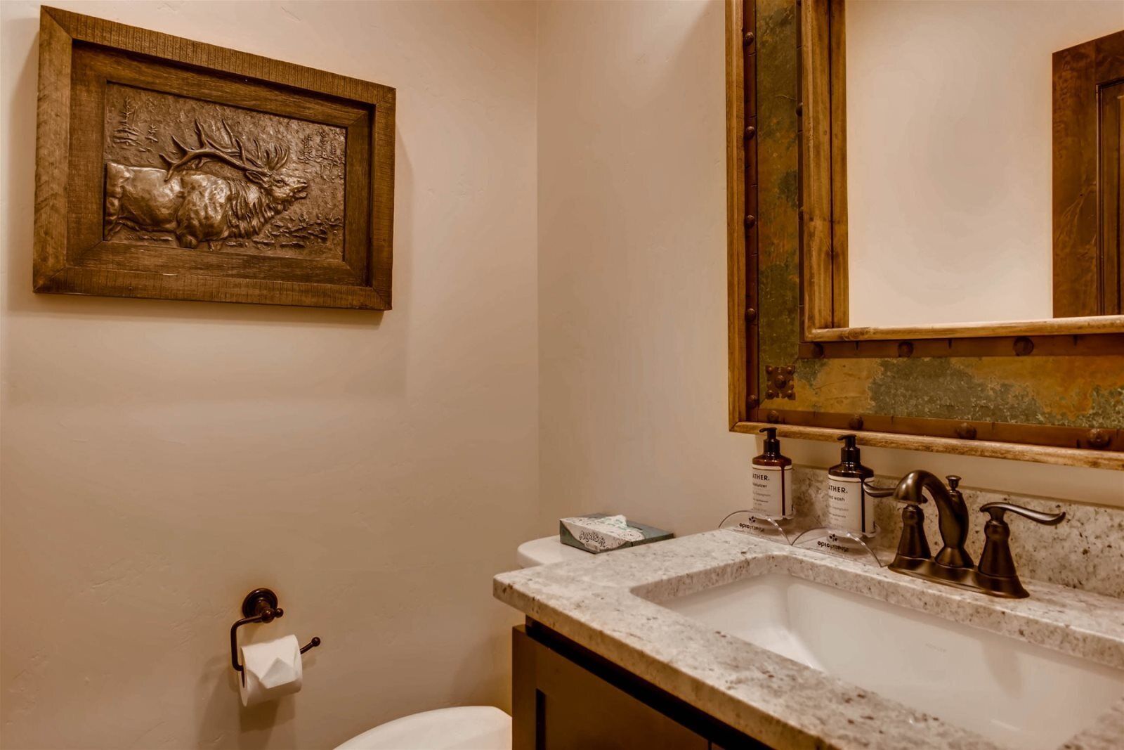 Une salle de bain avec un lavabo en marbre, une œuvre d’art encadrée en bois représentant un élan, et un porte-rouleau de papier toilette.