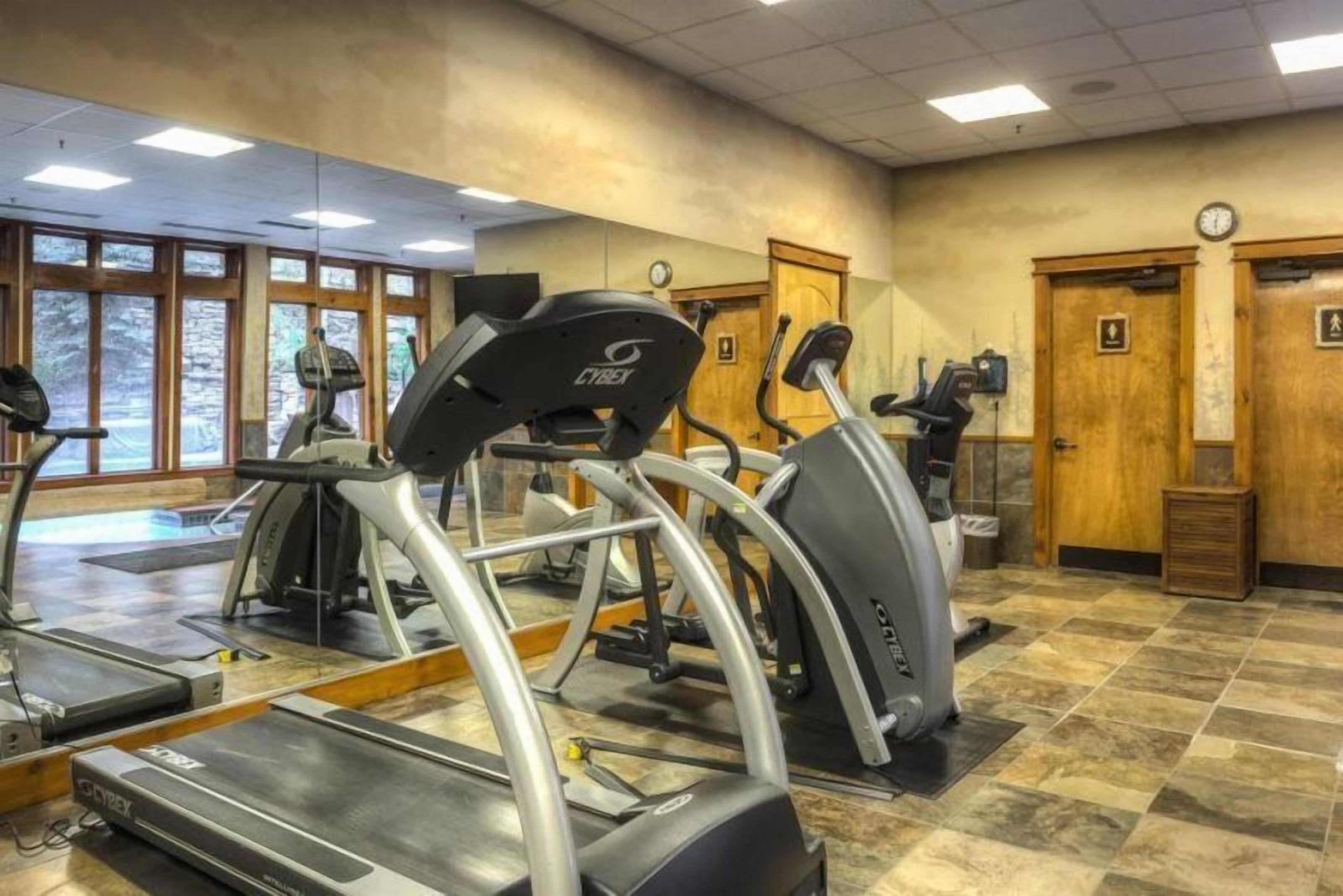 Ein Fitnessraum mit Laufbändern und Trainingsgeräten, großen Fenstern und Holztüren.