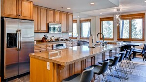 A modern kitchen with stainless steel appliances, wooden cabinets, a large island with bar stools, and large windows offering a view of the outdoors. - Premier 4 Bedroom Ski in, Ski out Vacation Rental at the Timbers With the Best Access to Skiing in Keystone (Keystone)