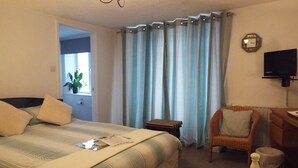 Habitación de hotel con cama, silla, escritorio, televisión y ventana con cortinas.