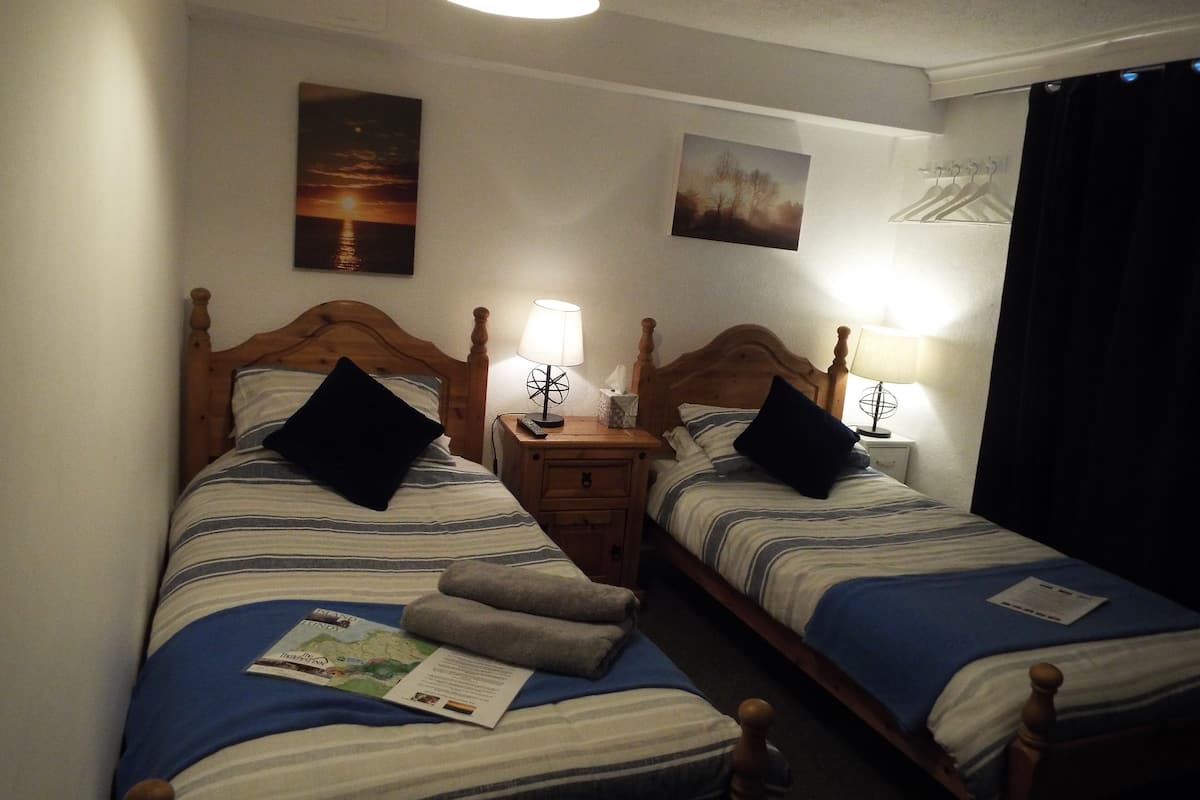 A hotel room with two single beds, each with a wooden headboard, a nightstand, a lamp, and a wall-mounted painting.
