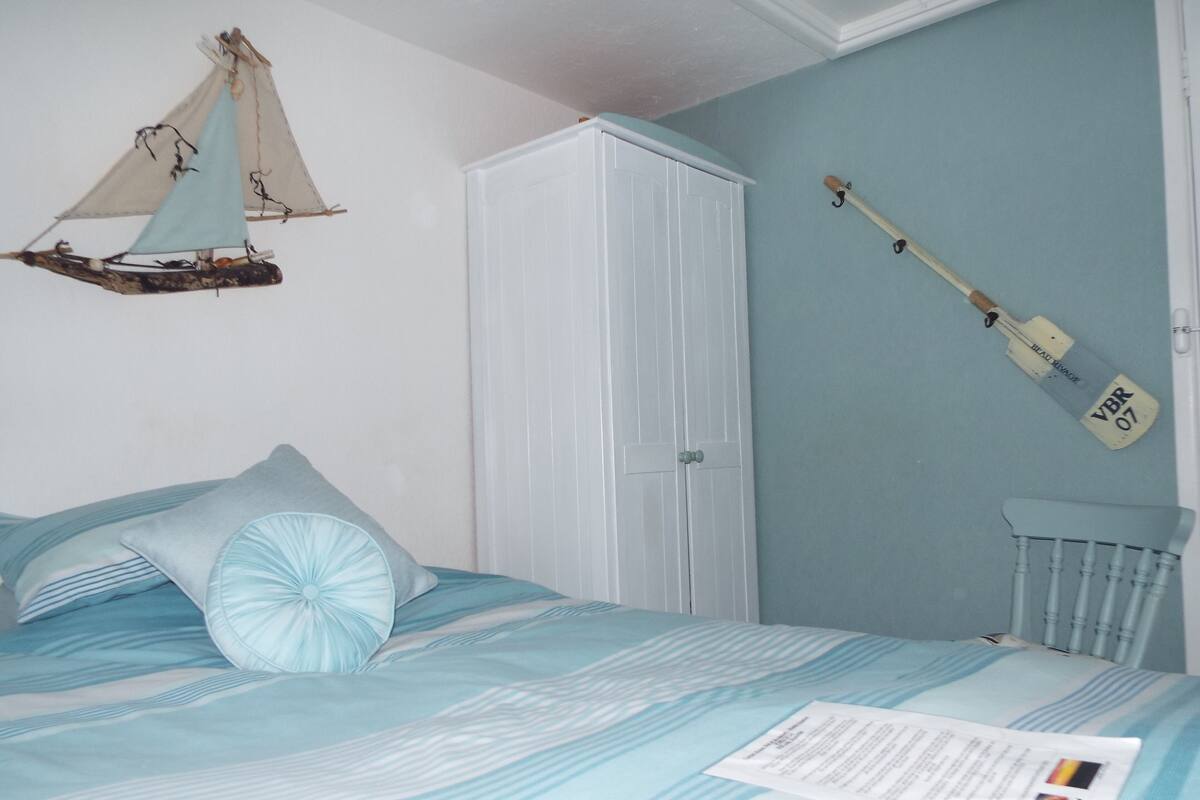 A bedroom with a bed, a wardrobe, a sailboat decoration, and a cricket bat.