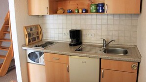 A compact kitchen with wooden cabinets, a built-in dishwasher, a coffee maker, and a sink. - Ferienhaus Windspiel (Lübbenau/Spreewald)