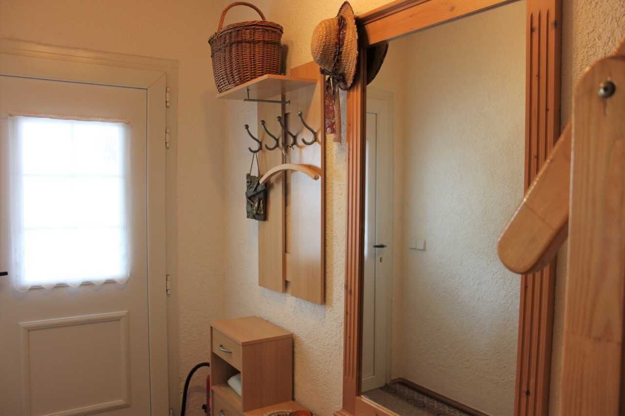 Un baño con puerta de madera, un espejo, un armario de madera y una ventana con cortina blanca.