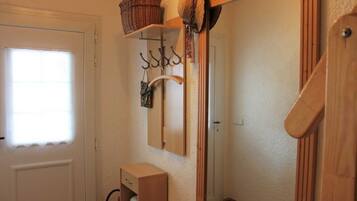 Un baño con puerta de madera, un espejo, un armario de madera y una ventana con cortina blanca.