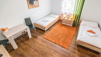 A small, well-lit room with two beds, a desk, and a chair.