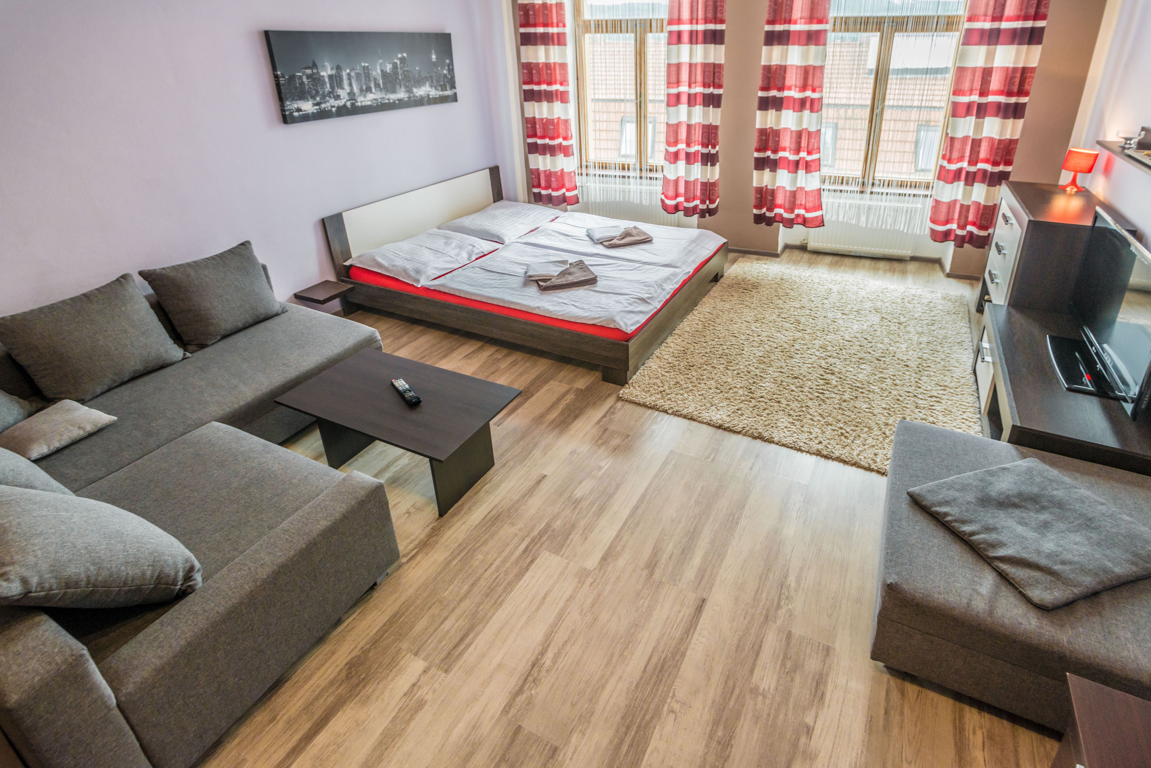 Een moderne woonkamer met een bank, een bed, een televisie en een raam met gordijnen.