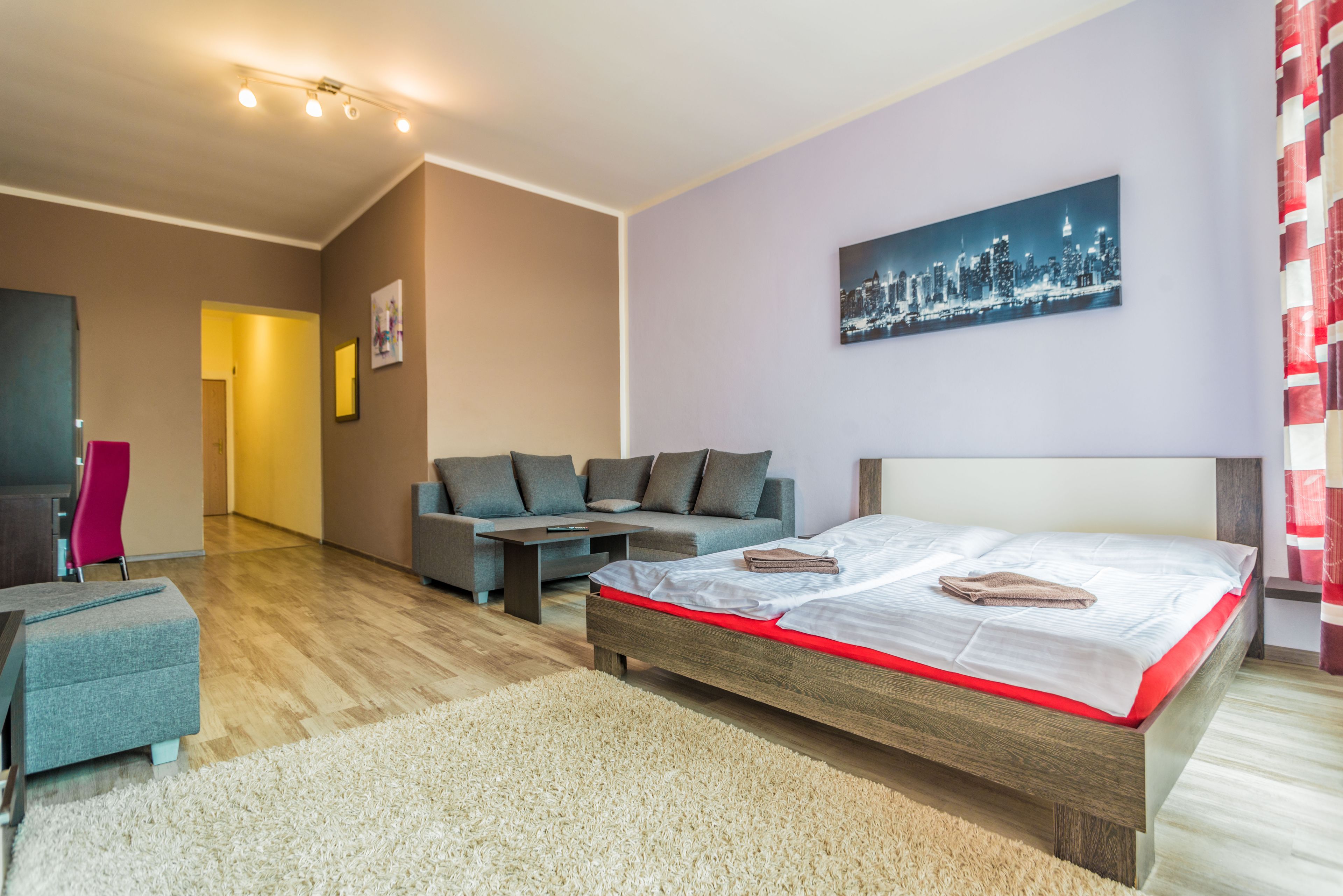 Ein modernes Schlafzimmer mit Bett, Sofa und einem Stadtbild an der Wand.