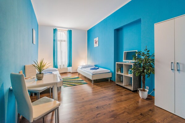 A compact room with a bed, a desk, a chair, a TV, and a potted plant. - Penzion TIME (Prešov)