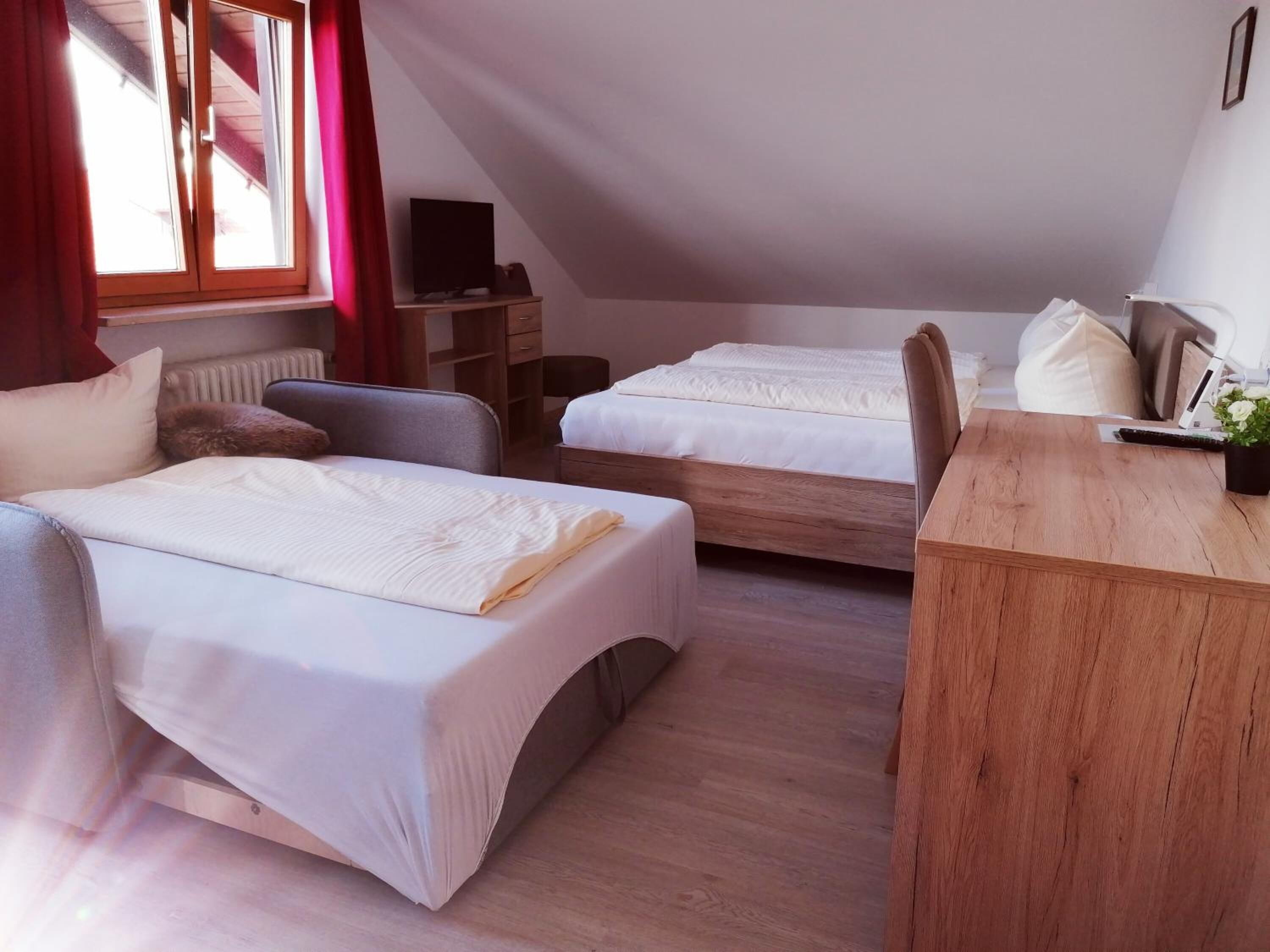 A room with two beds, a desk, a chair, a radiator, and a window with curtains.