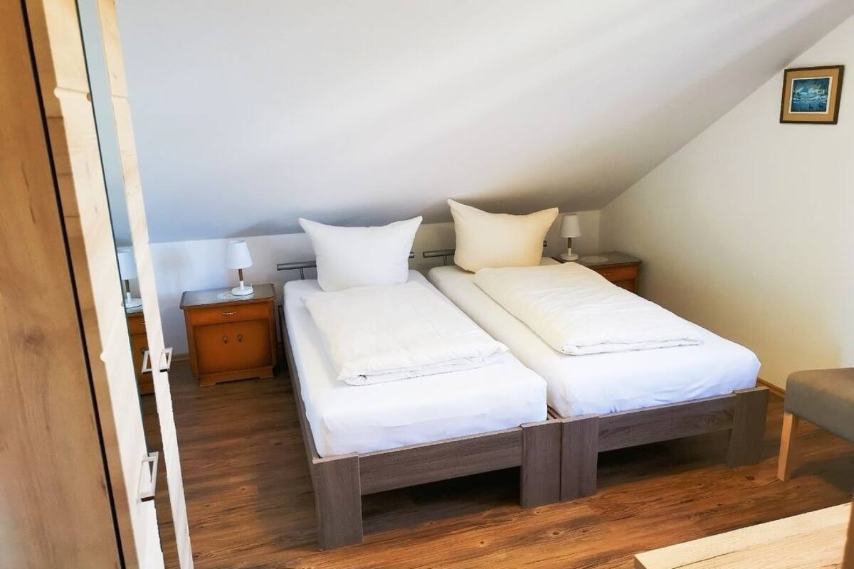 Un dormitorio con dos camas, suelo de madera, una mesita de noche y una mesilla auxiliar.