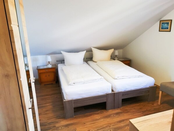 Un dormitorio con dos camas, suelo de madera, una mesita de noche y una mesilla auxiliar.