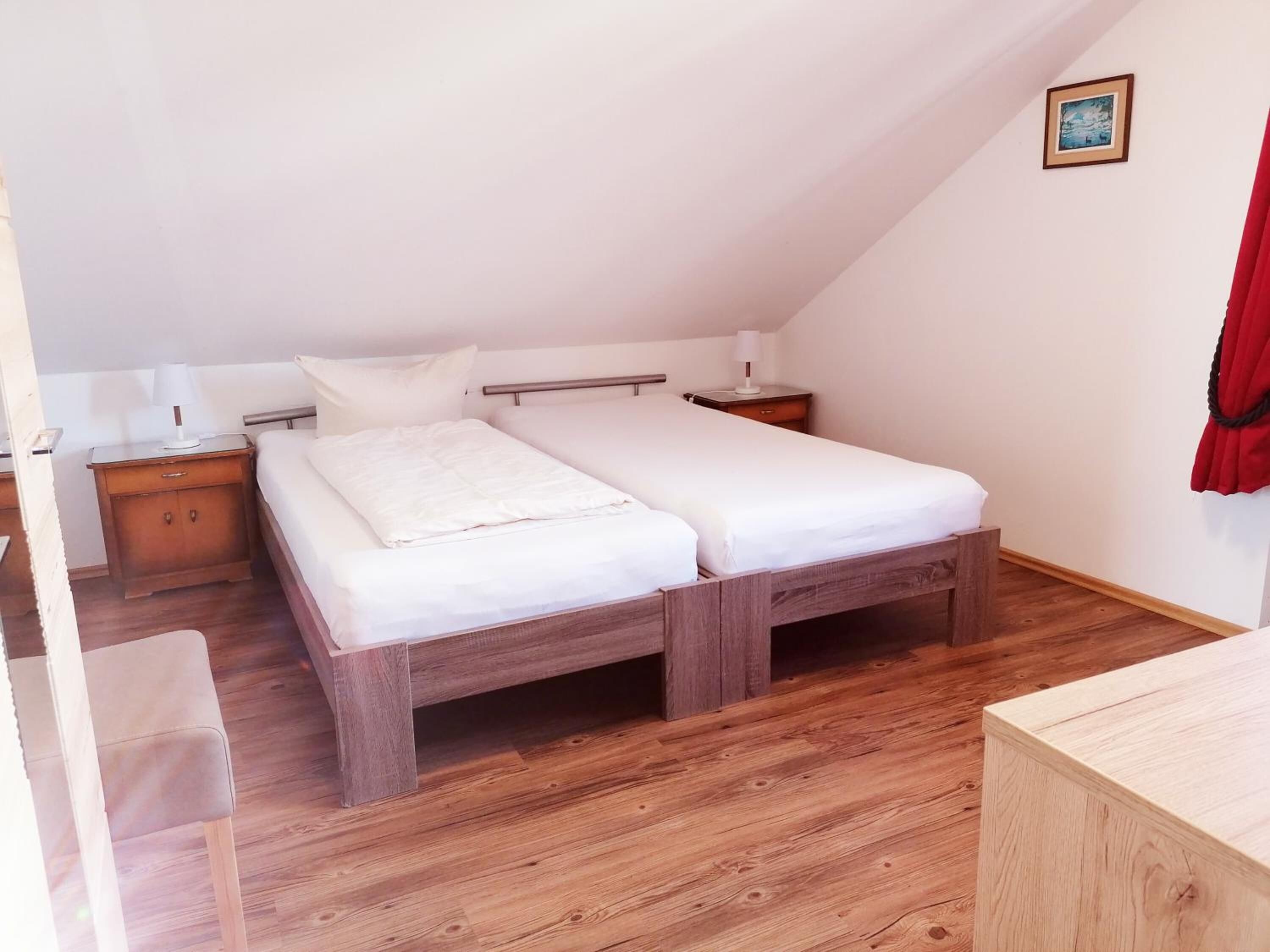 Une chambre individuelle avec un lit en bois, une table de chevet, une chaise et un petit bureau.