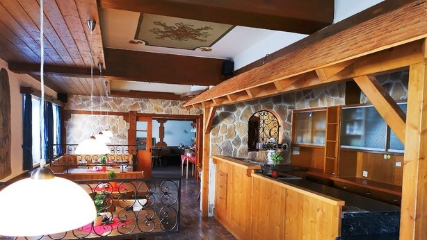 Een ruime kamer met een houten plafond, een stenen open haard, een houten bar en een gestreept banksofa.