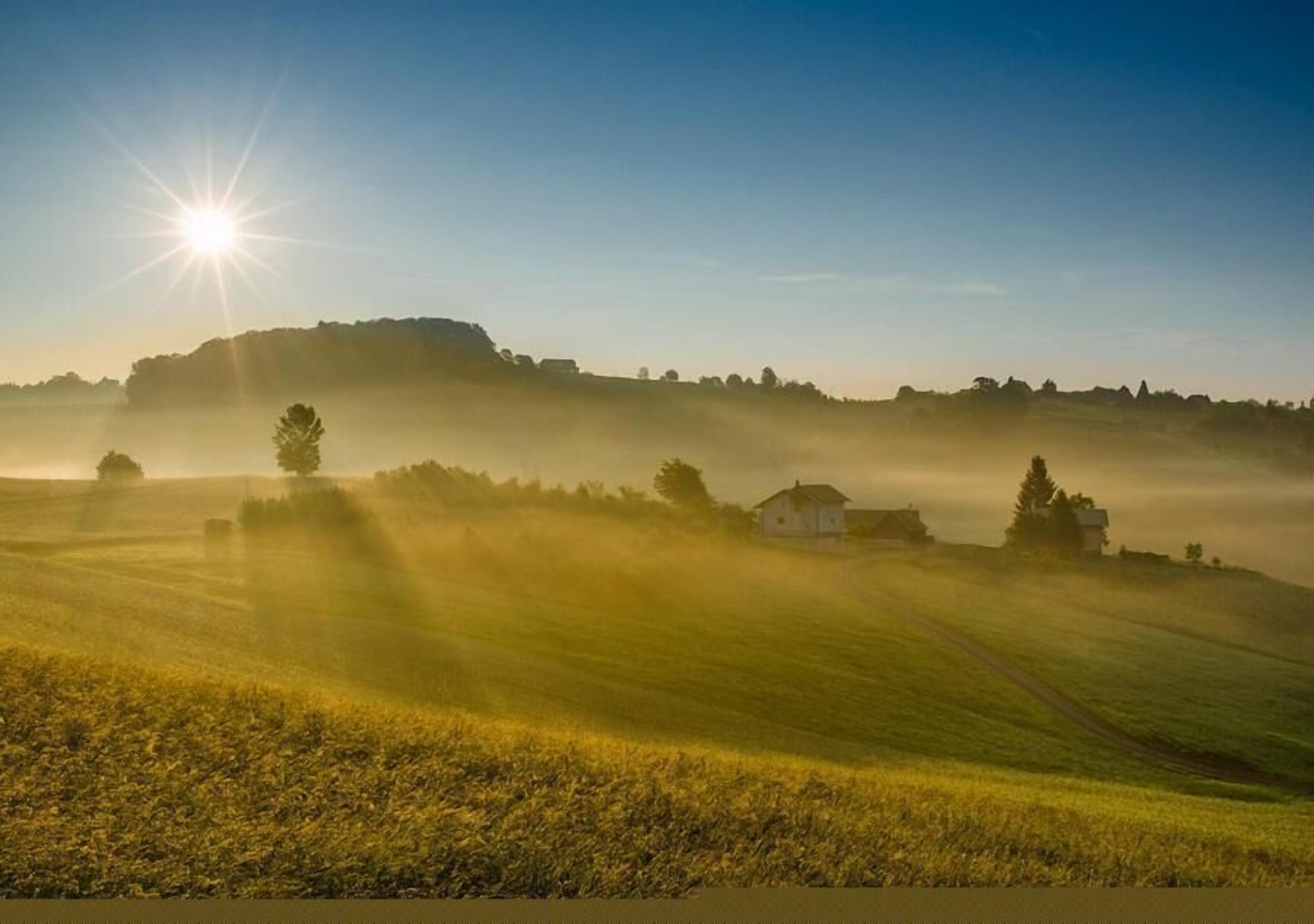Ländliche Landschaft mit einem Haus auf einem Hügel, umgeben von Feldern und Bäumen, unter blauem Himmel.